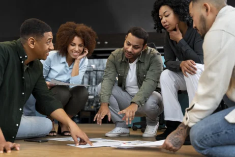 Equipe de colaboradores discutindo documentos no chão, em uma reunião descontraída e colaborativa, destacando a importância da gestão de pessoas para promover um ambiente de trabalho eficiente e engajado.