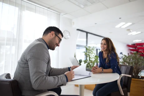 Candidata realizando uma entrevista de emprego com o recrutador. Ambos sentados, frente a frente, em uma conversa tranquila e sorridente.