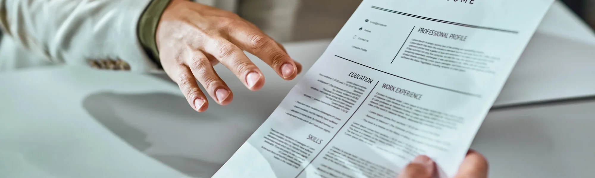 Foco na mão de um colaborador entregando seu currículo durante uma entrevista de emprego.